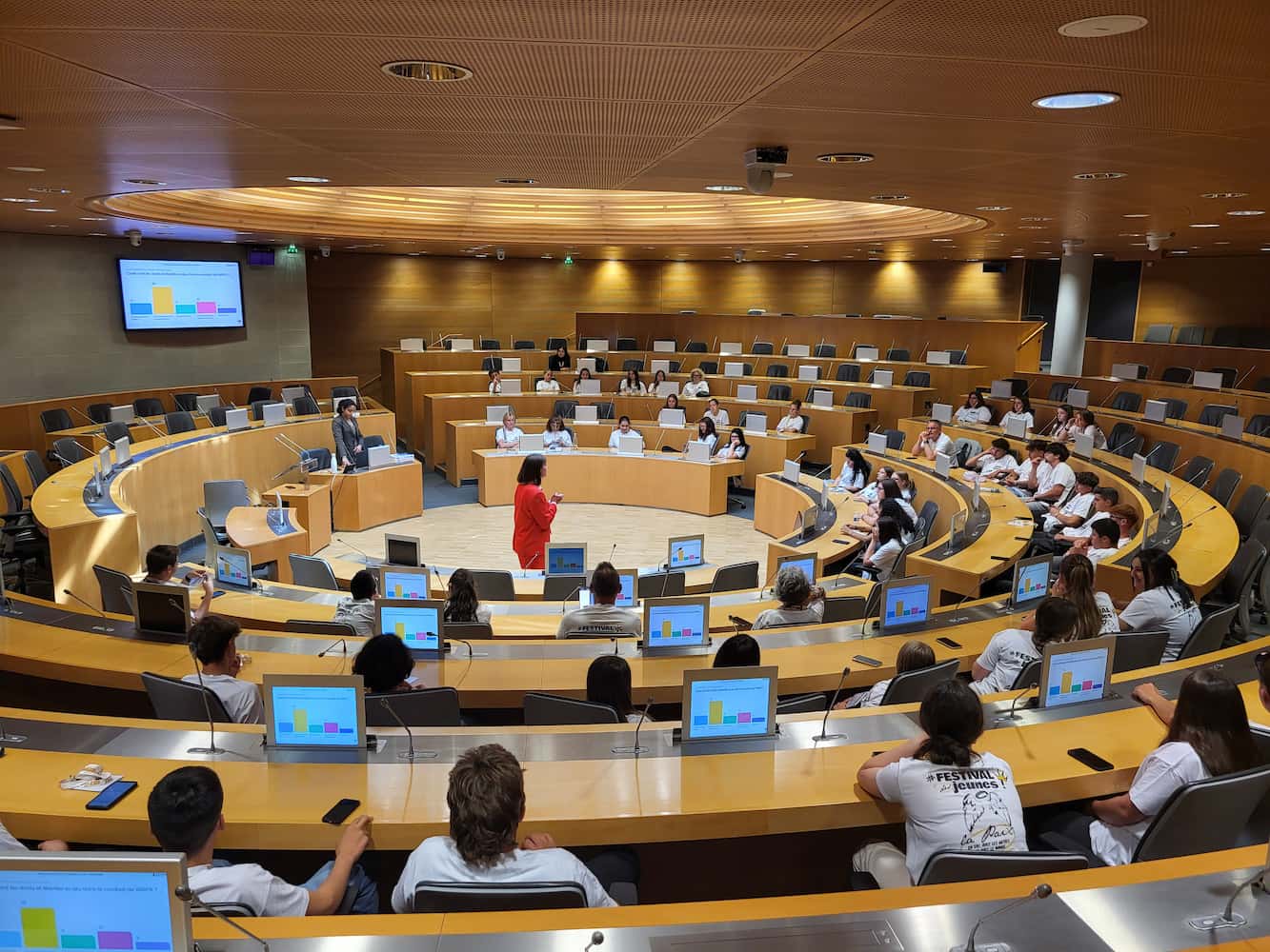 Séance plénière dans un grand hémicycle moderne, jeunes du Festival MFR 2025 en t-shirts blancs écoutant une présentation interactive à Strasbourg