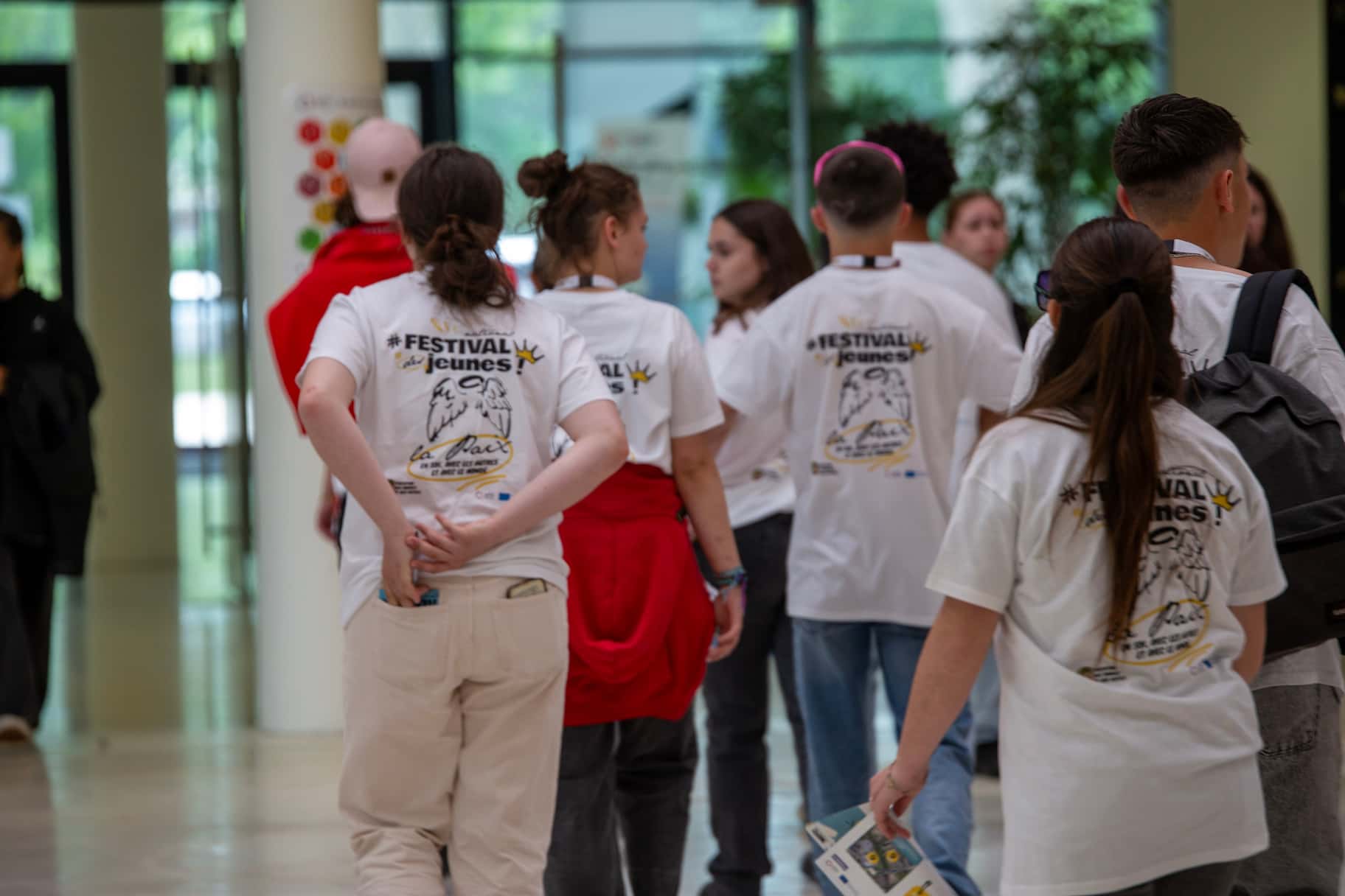 Groupe de jeunes marchant dans un hall lumineux, portant les t-shirts du Festival des Jeunes MFR 2025 avec le logo “La Paix” dans le dos